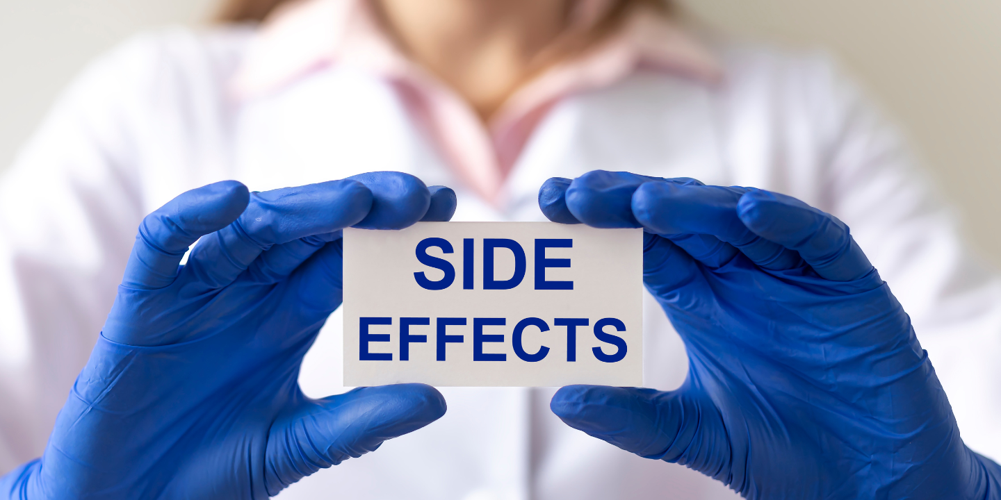 The image shows a person wearing blue gloves holding up a sign that reads "side effects." The person is likely a medical professional, such as a doctor or nurse, and the sign may be referring to the potential negative effects of a medication or treatment.