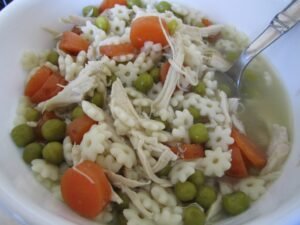 A bowl of homemade chicken noodle soup with shredded chicken, noodles, carrots, and peas.